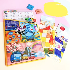 May include: A yellow folder with a cartoon image of a blue bus on the front. The folder has the text "Tayo The Little Bus" and "Tayo City Tour" on it. There are three smaller cards with cartoon images on them.