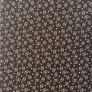 May include: Close-up of a fabric with a repeating pattern of white interlocking circles and small white dots on a dark brown background. The design is evenly spaced and creates a textured appearance. The fabric is likely used for clothing or home decor.
