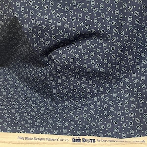 May include: Navy blue fabric with a repeating pattern of white dots and interlocking circles. The fabric has a slight sheen and is labeled "Riley Blake Designs Pattern C14175 BEE DOTS".