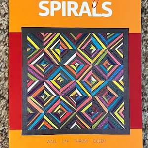 May include: An orange and red quilt pattern book titled "Swanky Spirals." The cover features a colorful quilt design with geometric patterns in various colors. The text at the bottom reads "Wall Lap Throw Queen" and "a fat quarter pattern by ChristaQuilts."
