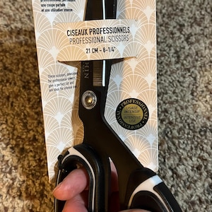 May include: Black and white professional sewing scissors, 8 1/4 inches long, with a black handle and white accents. The scissors are designed for professional sewers and intense use. The packaging includes the text "Professional Scissors".