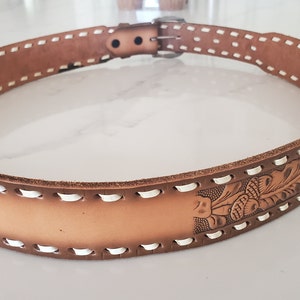 May include: A brown leather belt with white stitching and a floral design. The belt has a silver buckle.