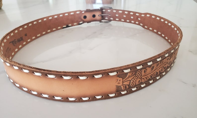 May include: A brown leather belt with white stitching and a floral design. The belt has a silver buckle.