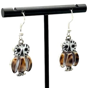 May include: A pair of silver owl earrings with brown and white shell inlays. The owls are hanging from silver hooks.