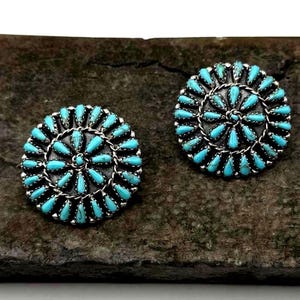 May include: A pair of turquoise and sterling silver earrings with a circular design. The earrings are made of small turquoise stones set in silver.