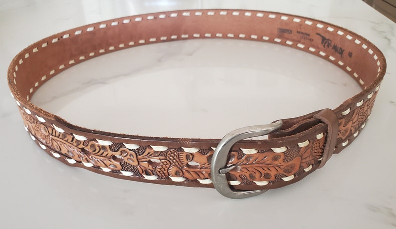 May include: A brown leather belt with white stitching and a silver buckle. The belt is decorated with a floral pattern.