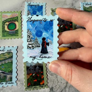 May include: A collection of decorative postage stamps featuring scenes from a fantasy world. One stamp shows a figure in a black robe and scarf with an owl, with the text "Hogwarts is my home." Other stamps depict landscapes and buildings.
