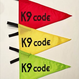 May include: Three triangular flags with black straps. The flags are red, yellow, and green. Each flag has the text "K9 code" printed in black.