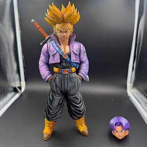 May include: A yellow-haired anime figure with a purple jacket and black pants holding a sword. The figure is standing on a gray surface. A separate purple head is also shown.