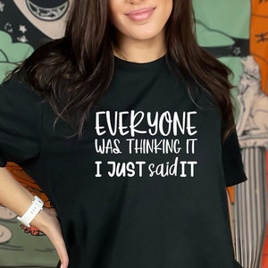 May include: Black t-shirt with the white text "EVERYONE WAS THINKING IT I JUST SAID IT". The shirt is a casual style, suitable for everyday wear. The background includes a tapestry with a wolf and floral design.