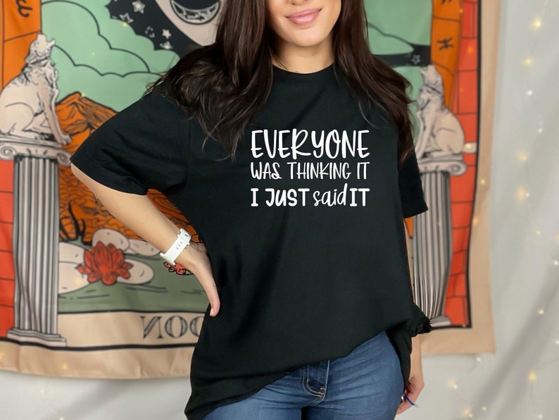 May include: Black t-shirt with the white text "EVERYONE WAS THINKING IT I JUST SAID IT". The shirt is a casual style, suitable for everyday wear. The background includes a tapestry with a wolf and floral design.