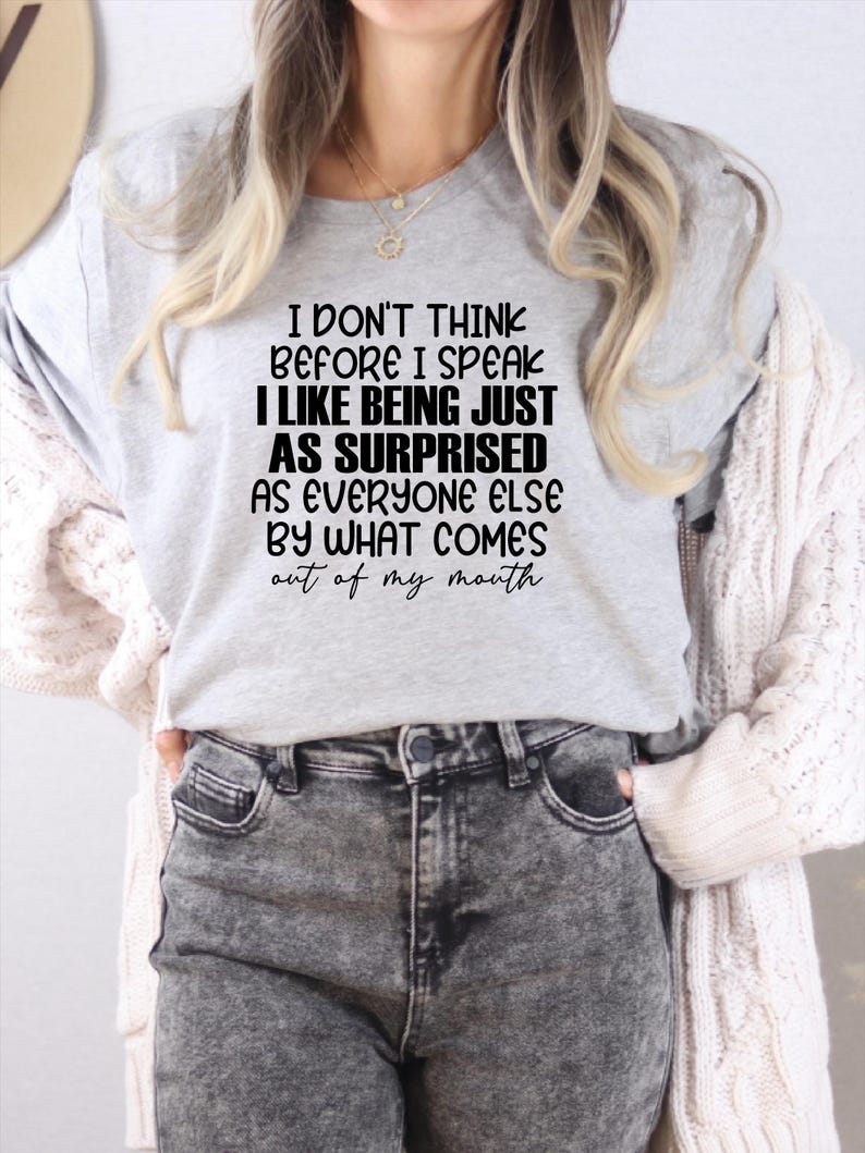 May include: A light gray t-shirt with the text "I DON'T THINK BEFORE I SPEAK I LIKE BEING JUST AS SURPRISED AS EVERYONE ELSE BY WHAT COMES out of my mouth." The shirt is paired with gray acid wash jeans.