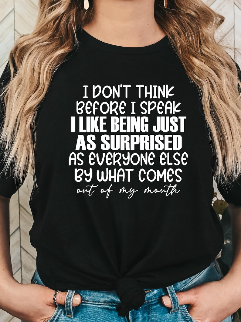 May include: Black t-shirt with white text. The text reads: "I DON'T THINK BEFORE I SPEAK I LIKE BEING JUST AS SURPRISED AS EVERYONE ELSE BY WHAT COMES out of my mouth."