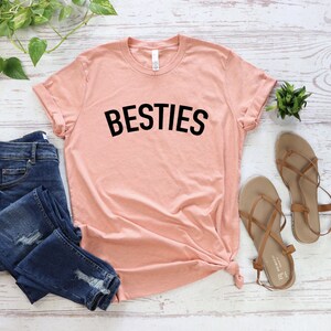 May include: A peach-colored t-shirt with the word "BESTIES" printed in black on the front.