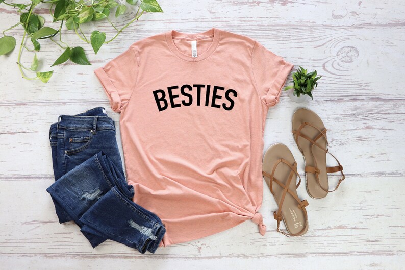 May include: A peach-colored t-shirt with the word "BESTIES" printed in black on the front.