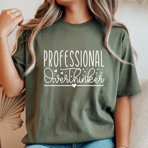 A woman wearing a green t-shirt with the text "Professional Overthinker" printed on it.
