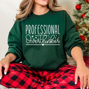 A woman wearing a green sweatshirt with the text "Professional Overthinker" printed on it, sitting in front of a Christmas tree.