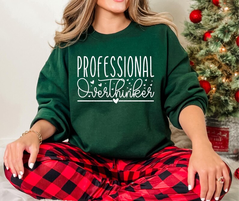 A woman wearing a green sweatshirt with the text "Professional Overthinker" printed on it, sitting in front of a Christmas tree.