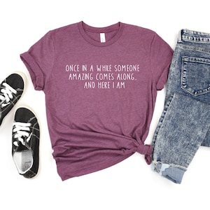 Może przedstawiać: Bordowy t-shirt z napisem "Once in a while someone amazing comes along... and here I am" w białym kolorze.