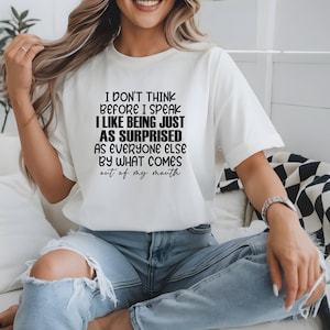 May include: White short-sleeve t-shirt with the text "I DON'T THINK BEFORE I SPEAK I LIKE BEING JUST AS SURPRISED AS EVERYONE ELSE BY WHAT COMES out of my mouth" in black. The shirt is paired with blue jeans.