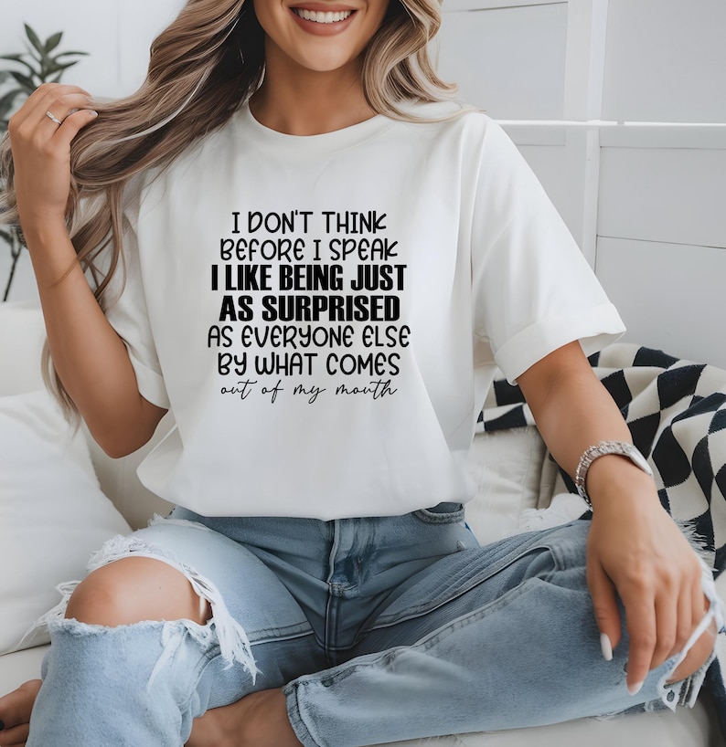 May include: White short-sleeve t-shirt with the text "I DON'T THINK BEFORE I SPEAK I LIKE BEING JUST AS SURPRISED AS EVERYONE ELSE BY WHAT COMES out of my mouth" in black. The shirt is paired with blue jeans.