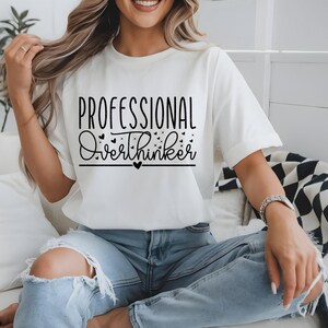 A woman wearing a white t-shirt with the text "Professional Overthinker" printed on it, sitting on a couch.