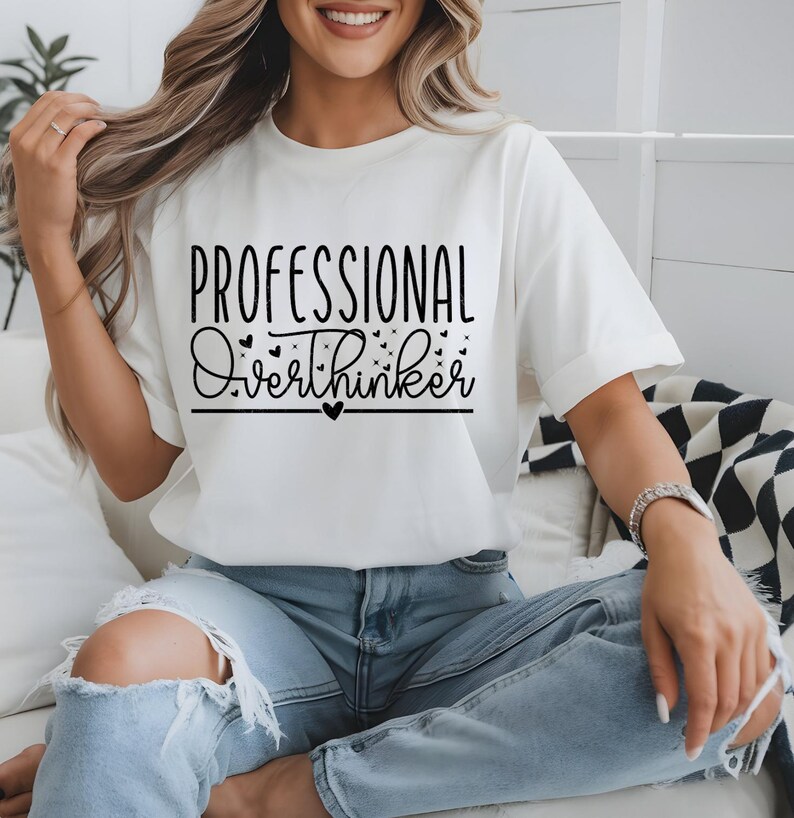 A woman wearing a white t-shirt with the text "Professional Overthinker" printed on it, sitting on a couch.