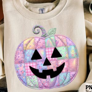 Może przedstawiać: Beżowa bluza z okrągłym dekoltem, ozdobiona dużym, centralnym nadrukiem dyni na Halloween. Dynia ma wzór patchworkowy wykonany z pastelowych tkanin w kwiaty, wzory paisley i kratkę, zwieńczony zieloną łodygą oraz listkiem.