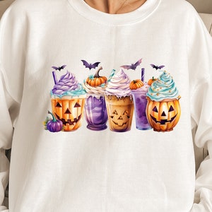 May include: White sweatshirt with a Halloween-themed design featuring four pumpkin-shaped cups with whipped cream and sprinkles. Each cup has a different colored base and a smiling pumpkin face.