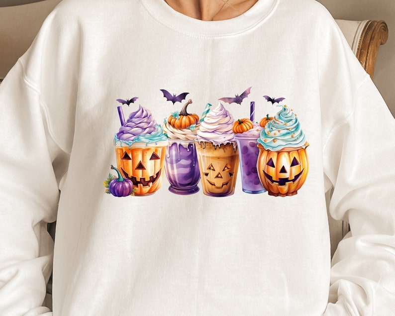 May include: White sweatshirt with a Halloween-themed design featuring four pumpkin-shaped cups with whipped cream and sprinkles. Each cup has a different colored base and a smiling pumpkin face.