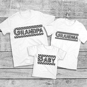 Peut inclure: Trois t-shirts blancs avec du texte &agrave; carreaux noirs qui se lit "GRANDPA", "GRANDMA" et "BABY". Les chemises sont dispos&eacute;es sur une surface &agrave; grain de bois clair. Les chemises sont &agrave; manches courtes.
