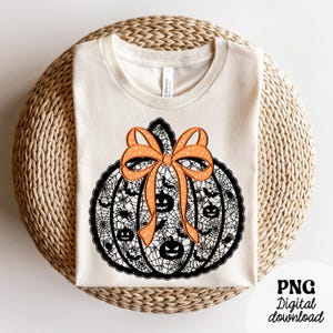 Może przedstawiać: Kremowa koszulka z motywem dyni na Halloween. Dynia jest czarna ze wzorem pajęczyny, twarzami jack-o'-lantern i nietoperzami. Pomarańczowa kokarda z białymi gwiazdkami zdobi g&oacute;rę. Tekst "PNG Digital download" znajduje się w prawym dolnym rogu.