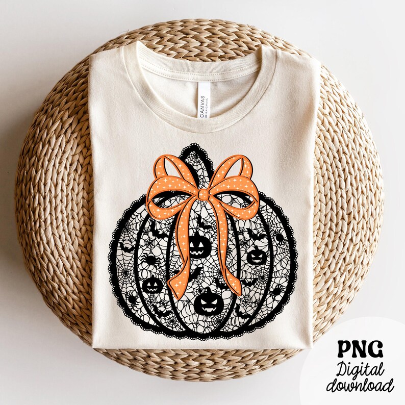 Może przedstawiać: Kremowa koszulka z motywem dyni na Halloween. Dynia jest czarna ze wzorem pajęczyny, twarzami jack-o'-lantern i nietoperzami. Pomarańczowa kokarda z białymi gwiazdkami zdobi g&oacute;rę. Tekst "PNG Digital download" znajduje się w prawym dolnym rogu.