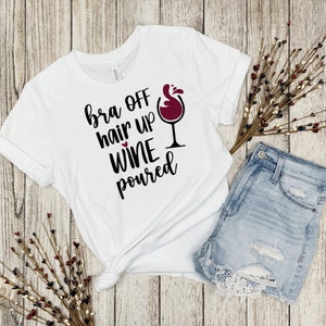 May include: White t-shirt with the text "bra off hair up wine poured" and a red wine glass graphic.