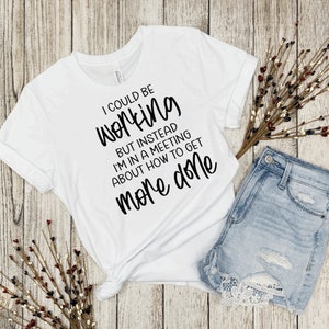 May include: White t-shirt with black text that reads "I could be working but instead I'm in a meeting about how to get more done."