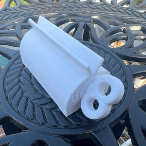Pode incluir: N&uacute;mero oito branco de pl&aacute;stico impresso em 3D com um furo no centro. O n&uacute;mero est&aacute; sobre uma mesa de metal preto com um padr&atilde;o decorativo.