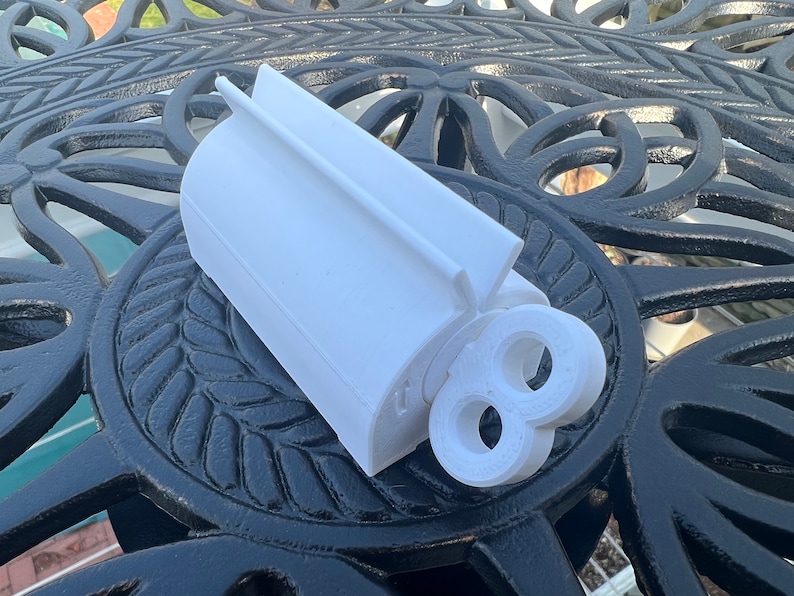 Pode incluir: N&uacute;mero oito branco de pl&aacute;stico impresso em 3D com um furo no centro. O n&uacute;mero est&aacute; sobre uma mesa de metal preto com um padr&atilde;o decorativo.