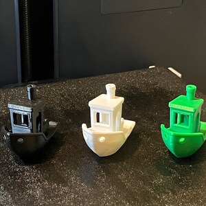 Pode incluir: Tr&ecirc;s rebocadores em miniatura impressos em 3D em preto, branco e verde. Os barcos t&ecirc;m uma pequena cabine com uma janela e uma chamin&eacute;.