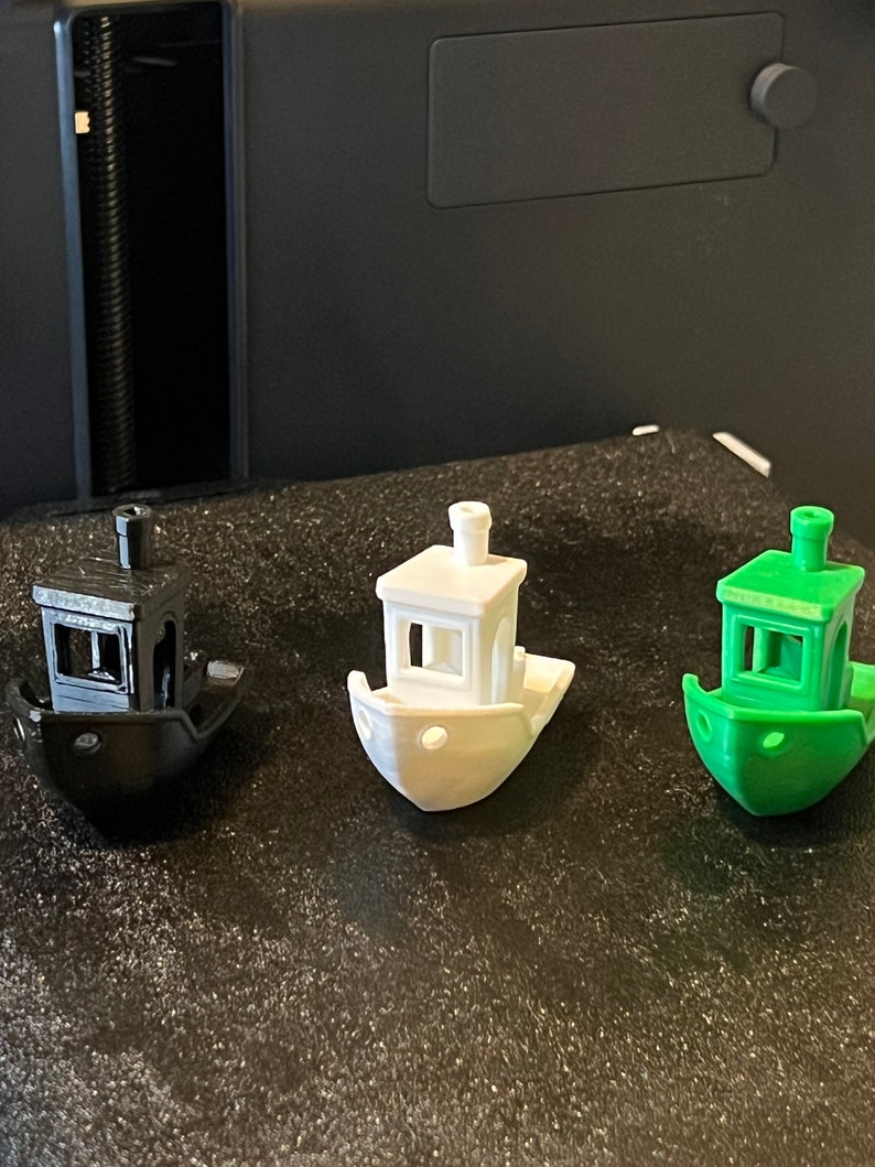 Pode incluir: Tr&ecirc;s rebocadores em miniatura impressos em 3D em preto, branco e verde. Os barcos t&ecirc;m uma pequena cabine com uma janela e uma chamin&eacute;.