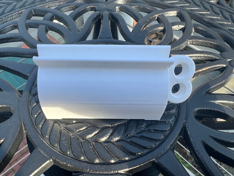Pode incluir: Vaso de pl&aacute;stico branco com formato arredondado e uma al&ccedil;a lateral. A al&ccedil;a tem dois furos.