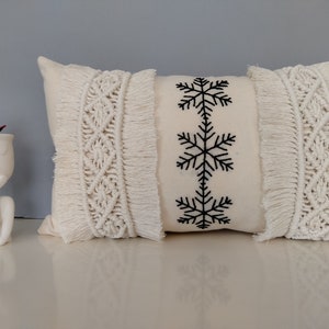 May include: A white throw pillow with a fringe border and three black embroidered snowflakes.
