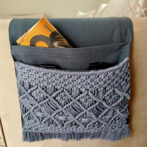 May include: Gray macrame hanging organizer with a gray fabric pocket and a magazine inside. The organizer is attached to a beige couch.