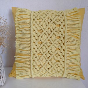 Könnte beinhalten: Ein gelbes Kissen mit einem weißen gehäkelten Muster und Fransenbesatz. Das Kissen ist aus Baumwolle und perfekt, um Ihrem Zuhause einen Hauch von Boho-Stil zu verleihen.