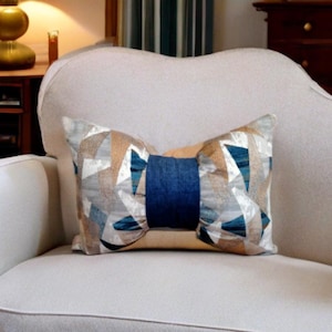 Peut inclure: Un fauteuil blanc avec un coussin de décoration géométrique bleu et beige. Le coussin a un nœud en velours bleu au centre.