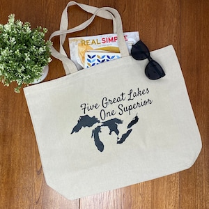 Peut inclure: Un sac fourre-tout en toile beige avec des anses noires et un graphique noir des Grands Lacs avec le texte "Five Great Lakes One Superior".