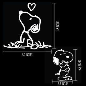K&ouml;nnte beinhalten: Zwei wei&szlig;e Snoopy-Aufkleber auf schwarzem Hintergrund. Einer zeigt Snoopy, der auf ein Herz blickt, 12,7 cm breit und 12,2 cm hoch. Der andere zeigt Snoopy, der sich selbst umarmt, 6,9 cm breit und 10,7 cm hoch.