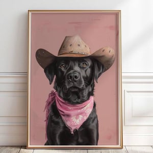 Könnte beinhalten: Gerahmtes Porträt eines schwarzen Labrador Retrievers mit braunem Cowboyhut und rosa Bandana. Der Hund ist vor einem rosa Hintergrund zentriert, der Rahmen ist goldfarben.