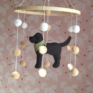 May include: A handmade baby mobile featuring a black Labrador silhouette with a green collar, suspended from a wooden hoop. The mobile includes white and tan felt balls hanging at different lengths, creating a whimsical nursery decoration.