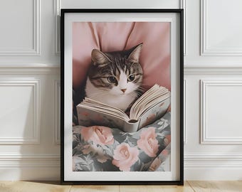 May include: A framed print of a tabby cat reading a book. The cat is resting on a floral blanket and a pink pillow. The open book is the focal point. The artwork is presented in a black frame, suitable for home decor.