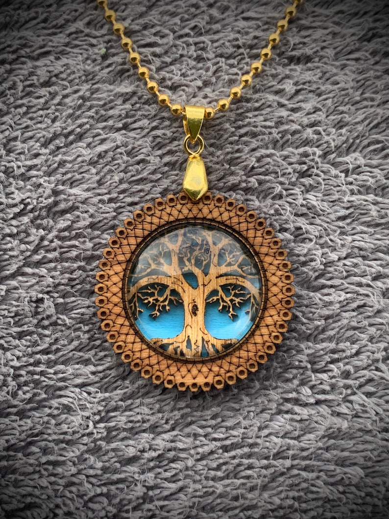 Pu&ograve; includere: Una collana con catena dorata con un ciondolo in legno con un design ad albero della vita blu e marrone.